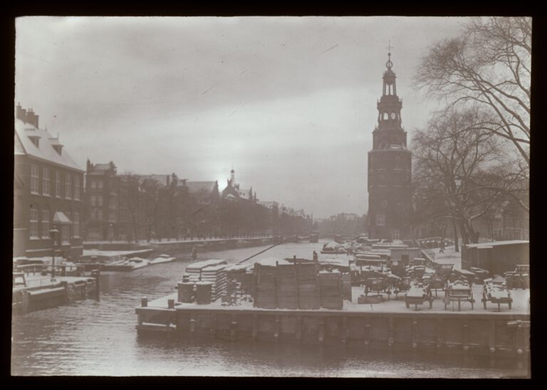 Lantaarnplaatje A35 uit de serie '40 jaar Amsterdam. De ziel der stad' - Oudeschans met Montelbaanstoren in de winter gezien vanaf de Prins Hendrikkade. Rechts de Kalkmarkt.