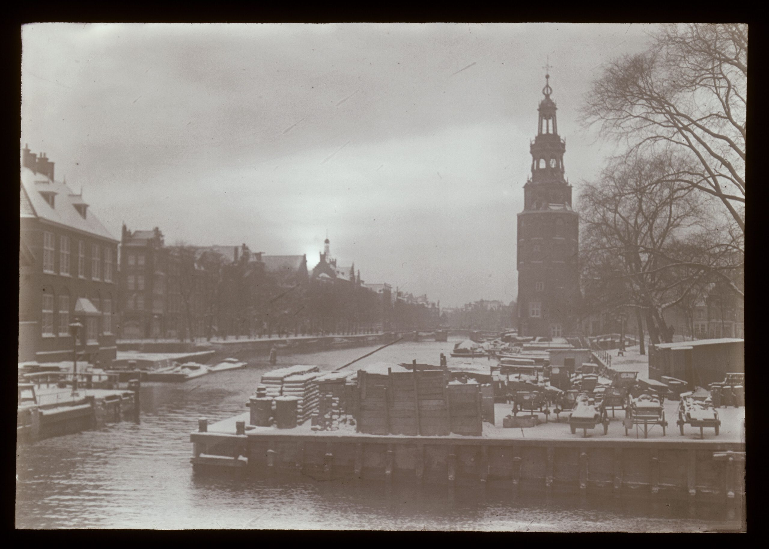Lantaarnplaatje A35 uit de serie '40 jaar Amsterdam. De ziel der stad' - Oudeschans met Montelbaanstoren in de winter gezien vanaf de Prins Hendrikkade. Rechts de Kalkmarkt.